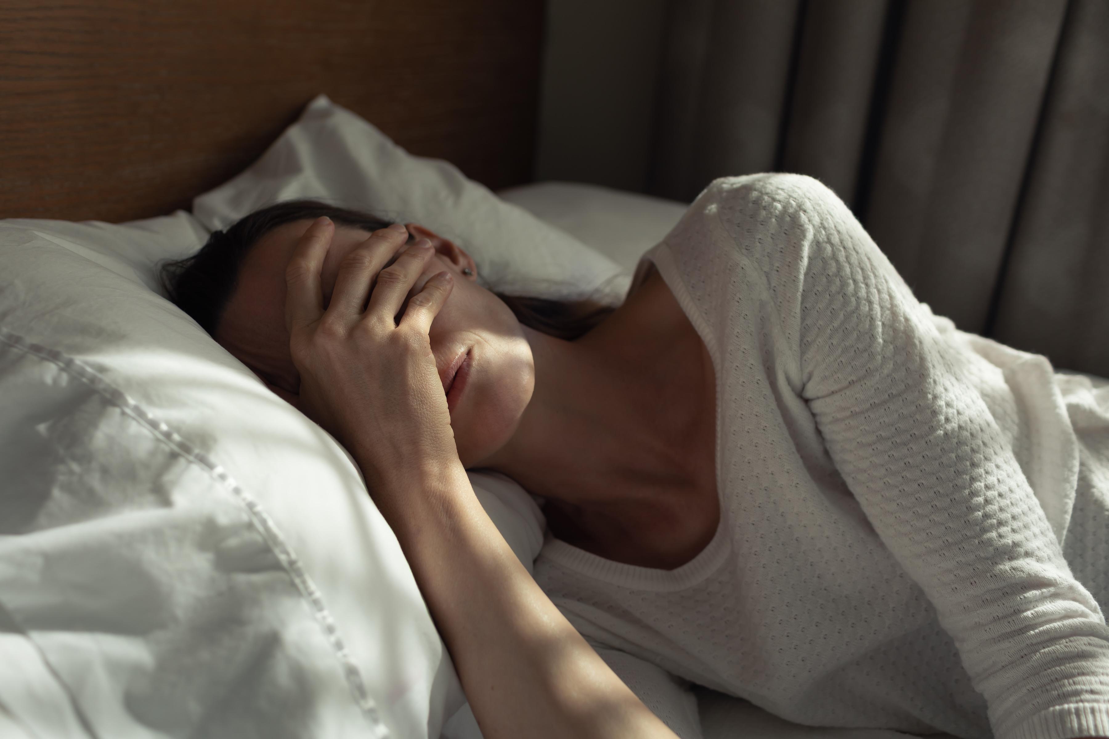 Photo of a woman sleeping in bed covering her face with her hand